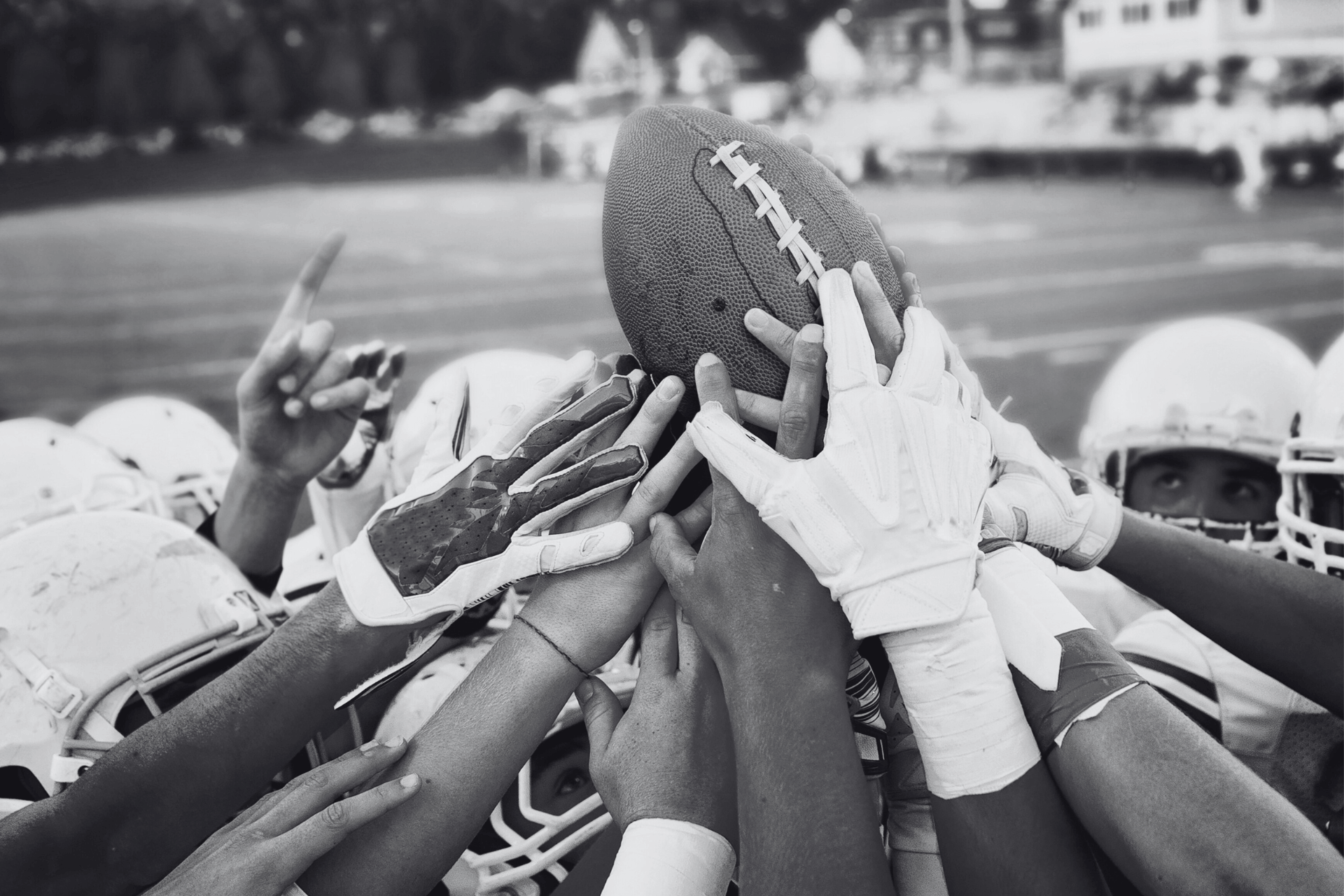 Football players' hands in a huddle holding a football.